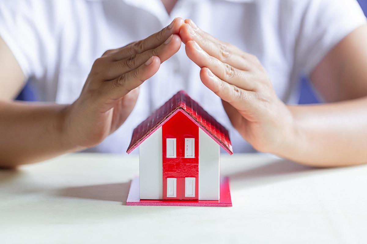 hands shielding a model house